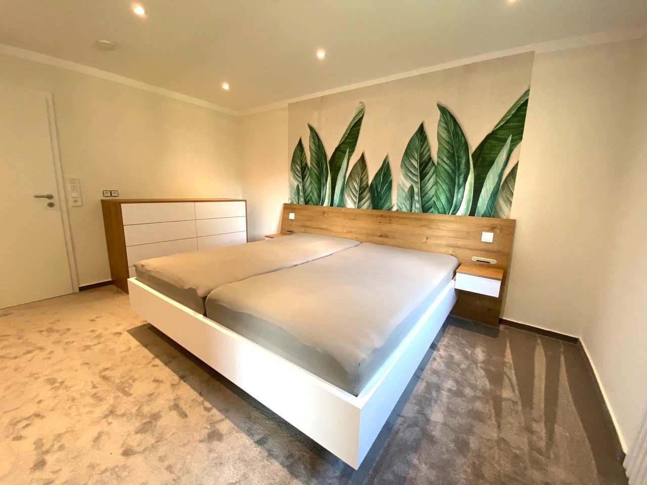 Bett mit Kopfteil und Kommode im Hintergrund
