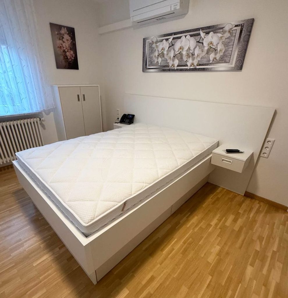 Weißes Bett mit Kopfteil und Nachttischen