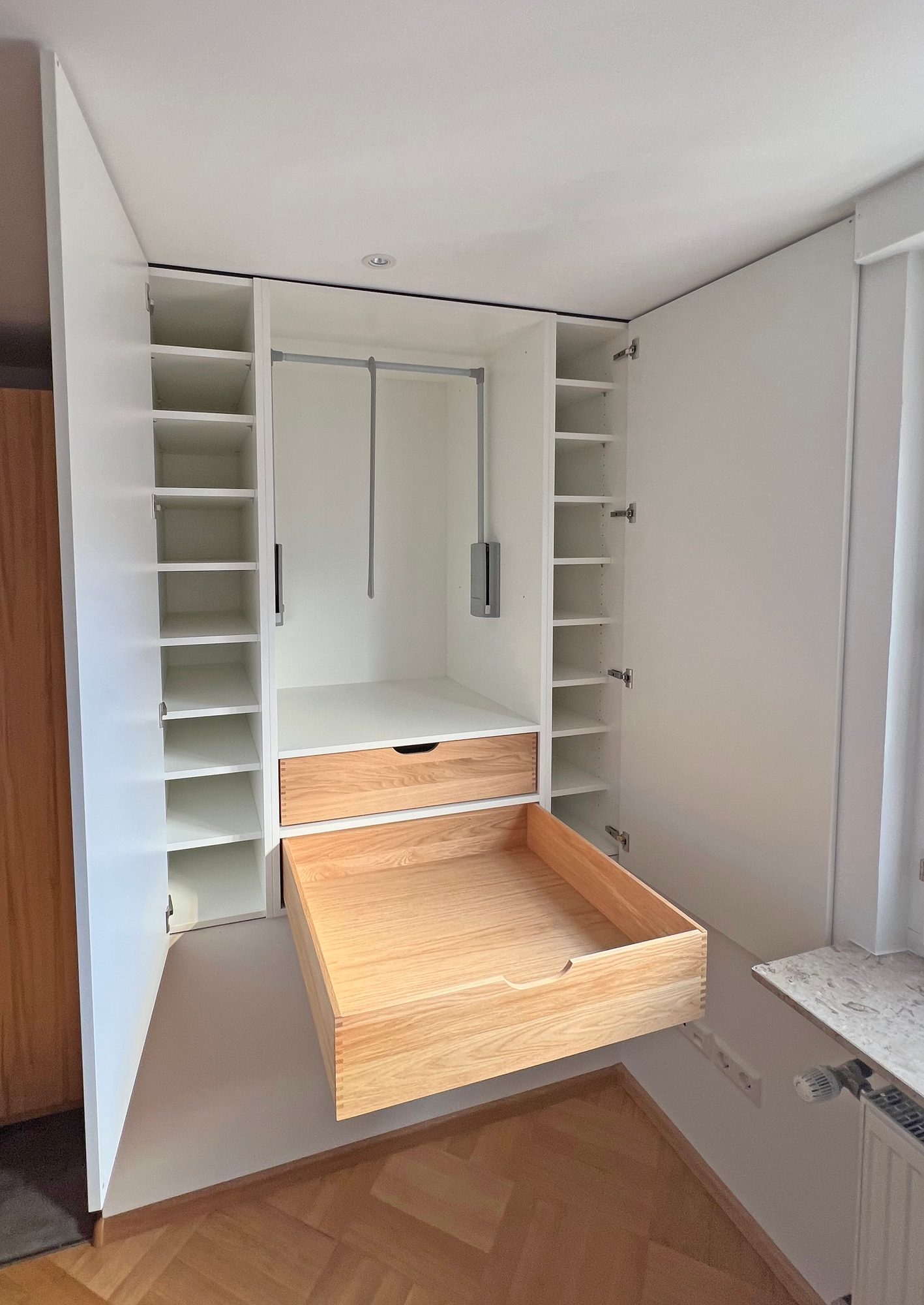 Einbauschrank mit Kleiderliften und geöffnetem Schubkasten in Holzoptik