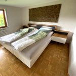 Weißes Bett mit beleuchtetem Kopfteil und Nachttischen in Holzoptik