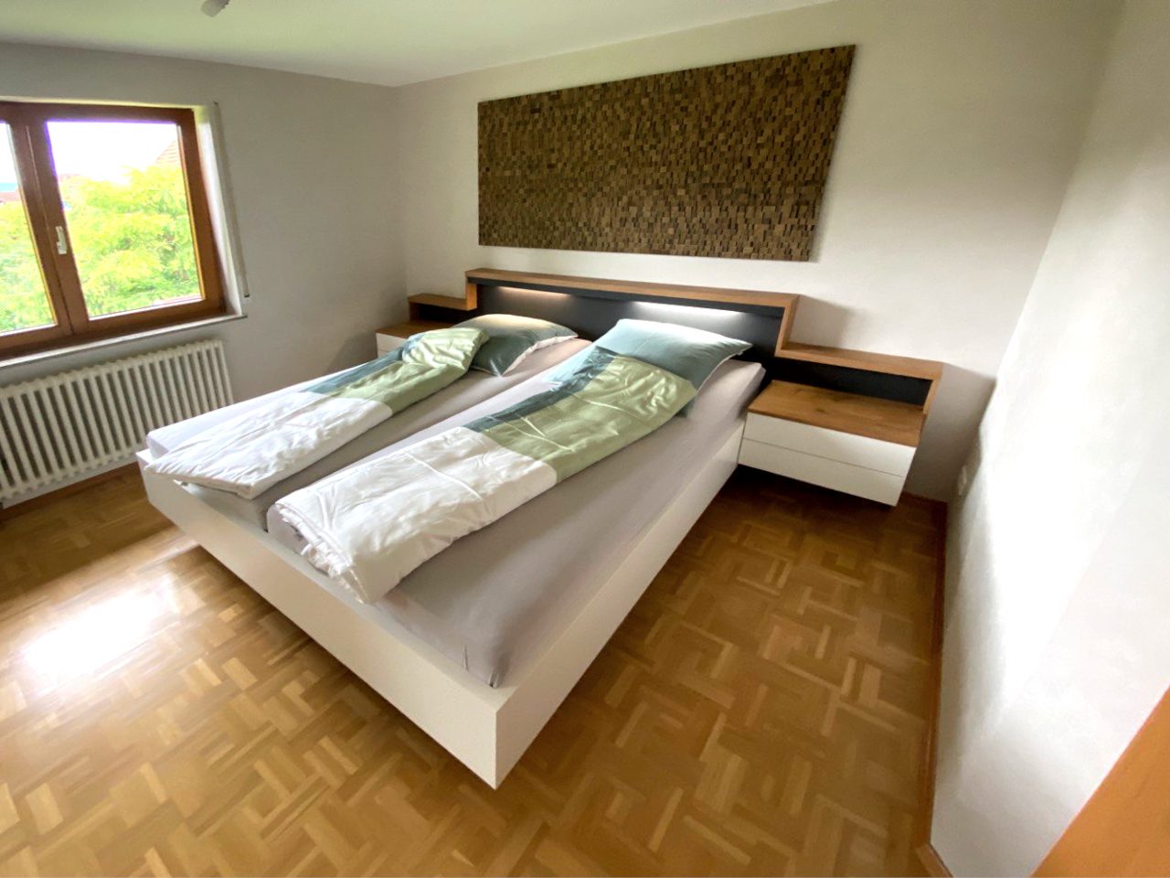 Weißes Bett mit beleuchtetem Kopfteil und Nachttischen in Holzoptik