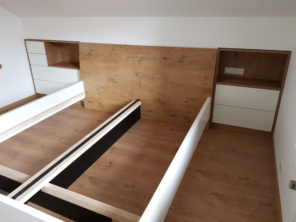 Rückwand mit Nischen und Schubladen neben dem Bett