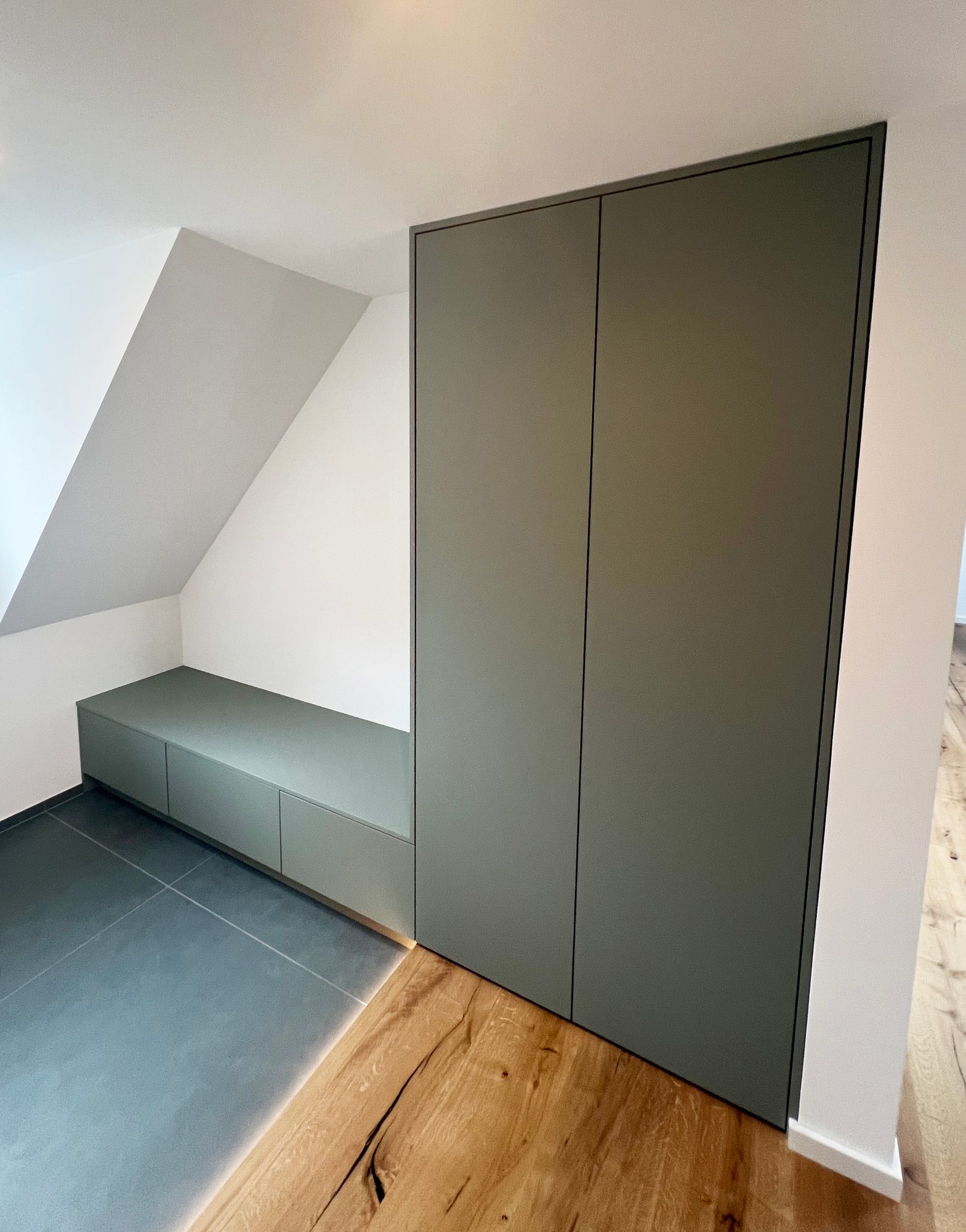 Graugrüner Hochschrank und niedrige Bank unter der Dachschräge