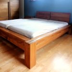 Holzbett mit hohem Kopfteil vor blauer Wand