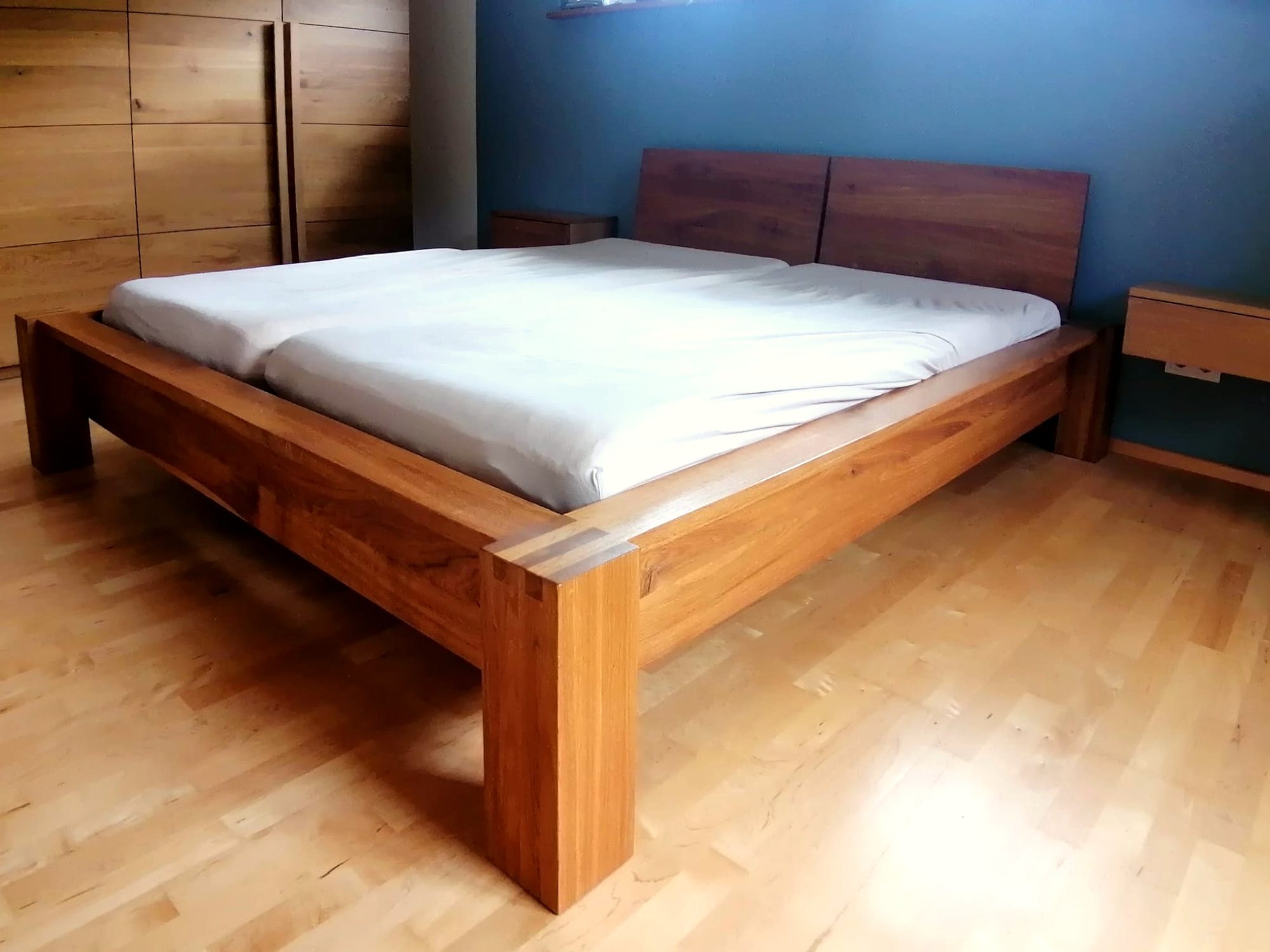 Holzbett mit hohem Kopfteil vor blauer Wand