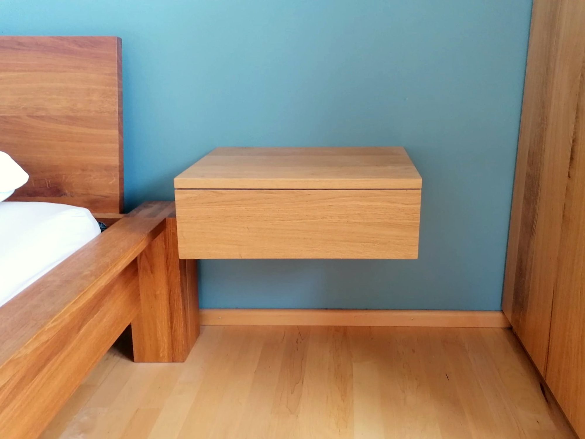 Schwebender Nachttisch aus Holz neben dem Bett