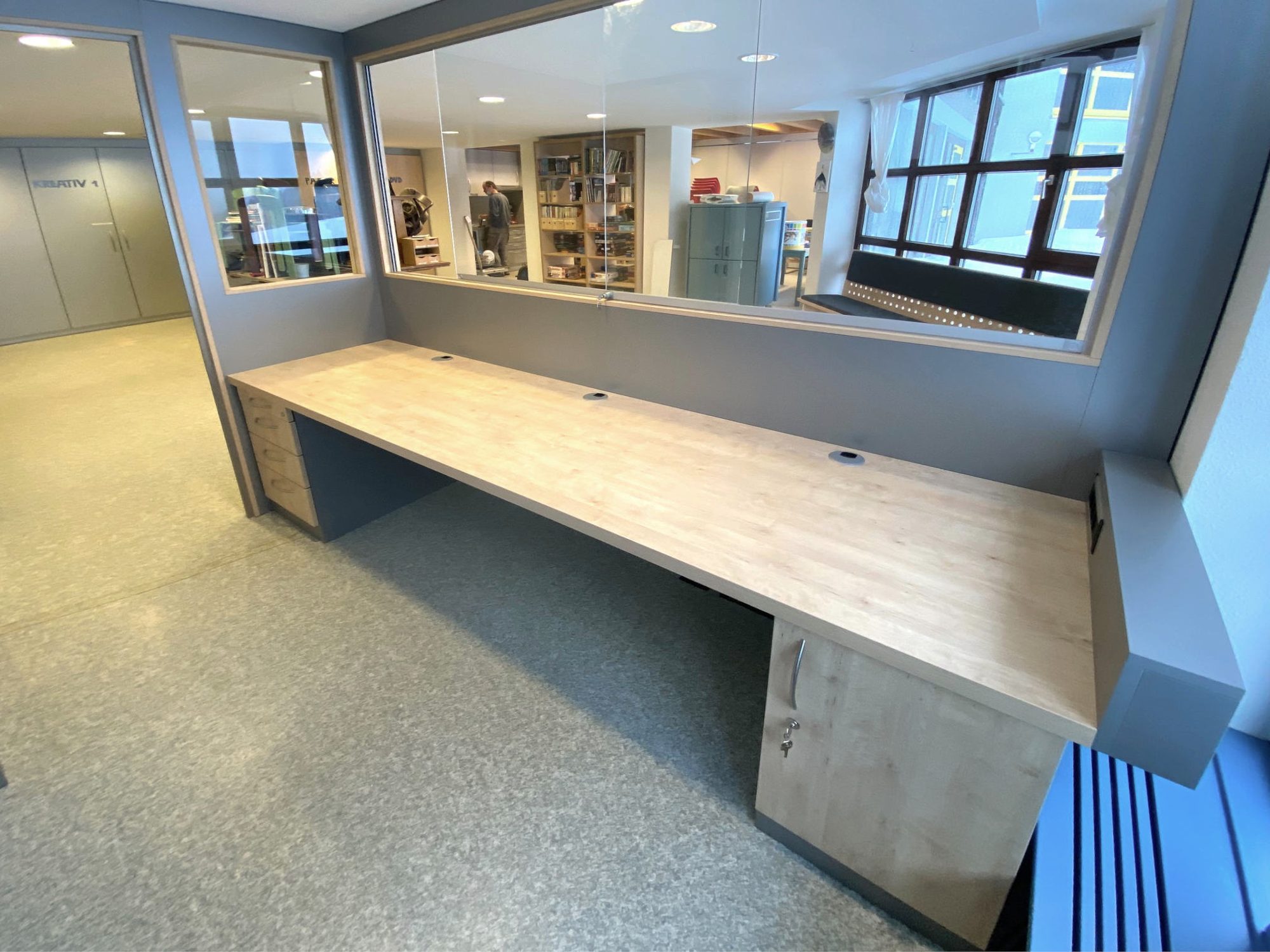Langer Arbeitstisch in Holzoptik an einer Glaswand