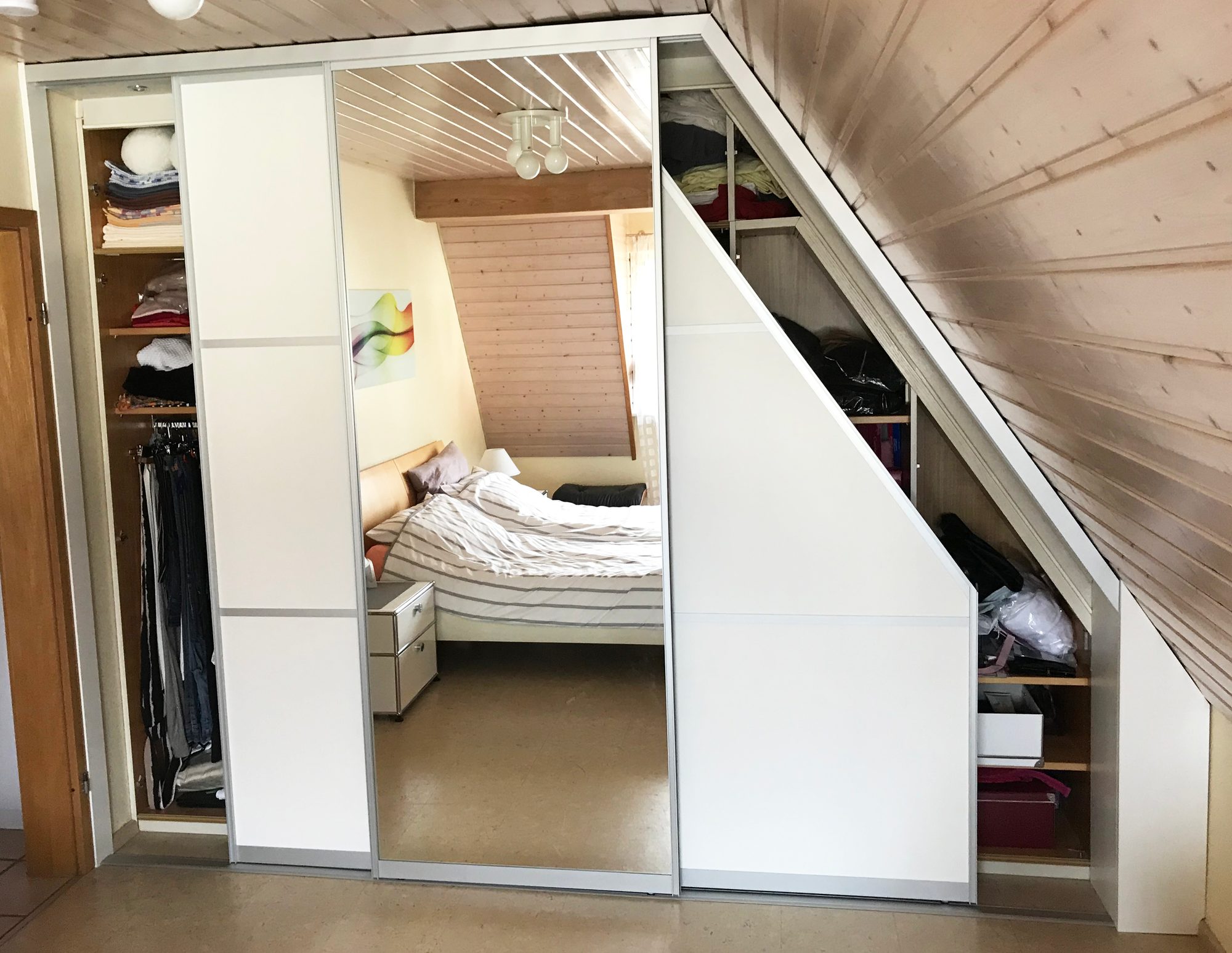 Geöffneter Schrank mit Kleiderstangen unter der Schräge