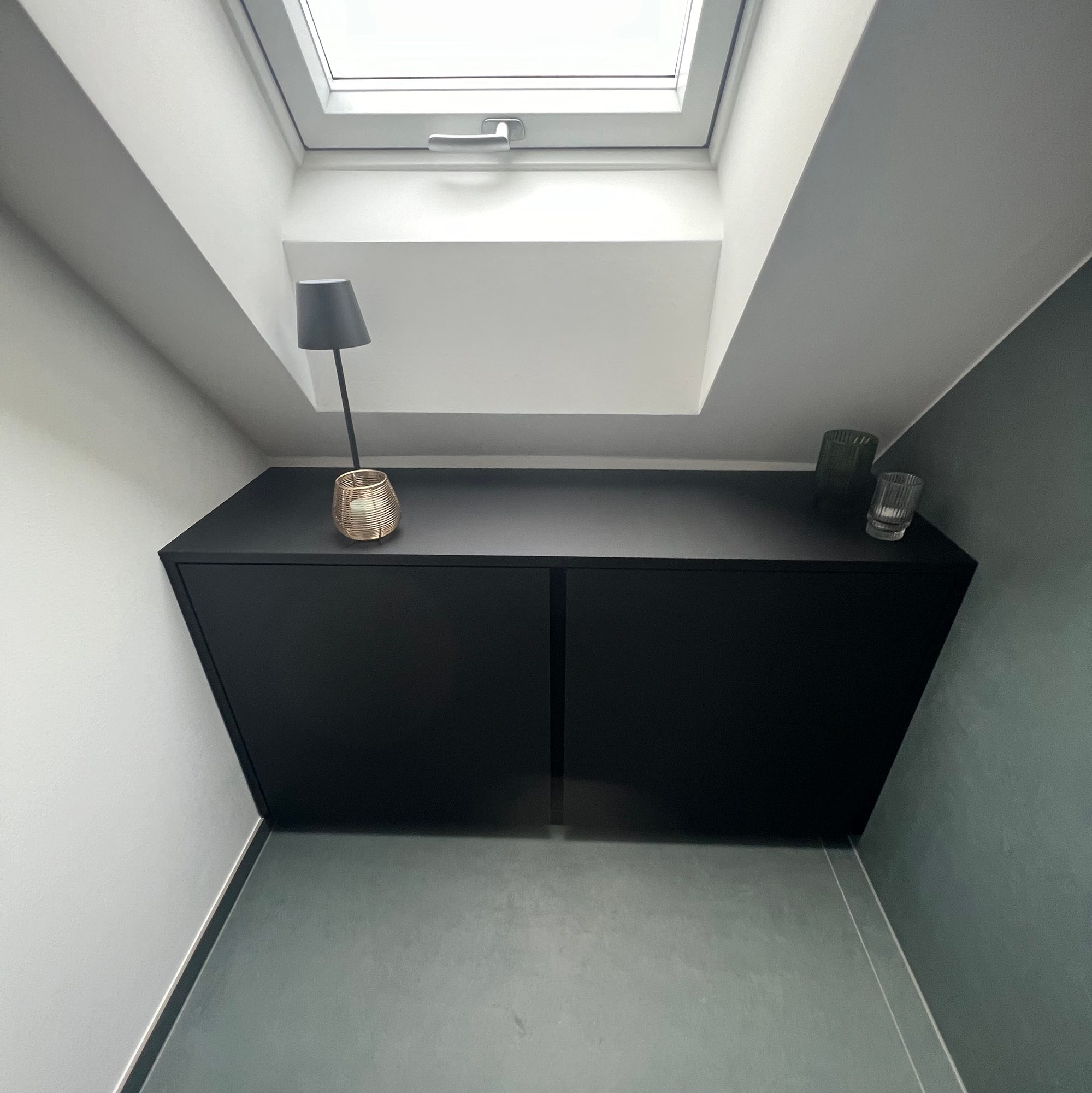 Mattschwarzes Sideboard unter dem Dachfenster