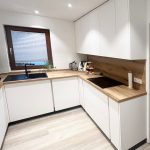 Weiße Eckküche mit Holzrückwand unter dem Fenster